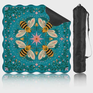 May include: A teal yoga mat with a floral and bee design. The mat features four bees around a central starburst, surrounded by flowers and foliage. A black carrying bag is included, offering convenient storage and transport.