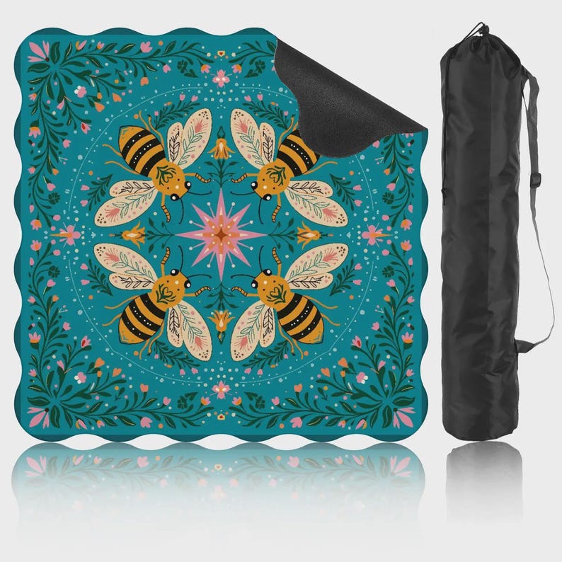 May include: A teal yoga mat with a floral and bee design. The mat features four bees around a central starburst, surrounded by flowers and foliage. A black carrying bag is included, offering convenient storage and transport.