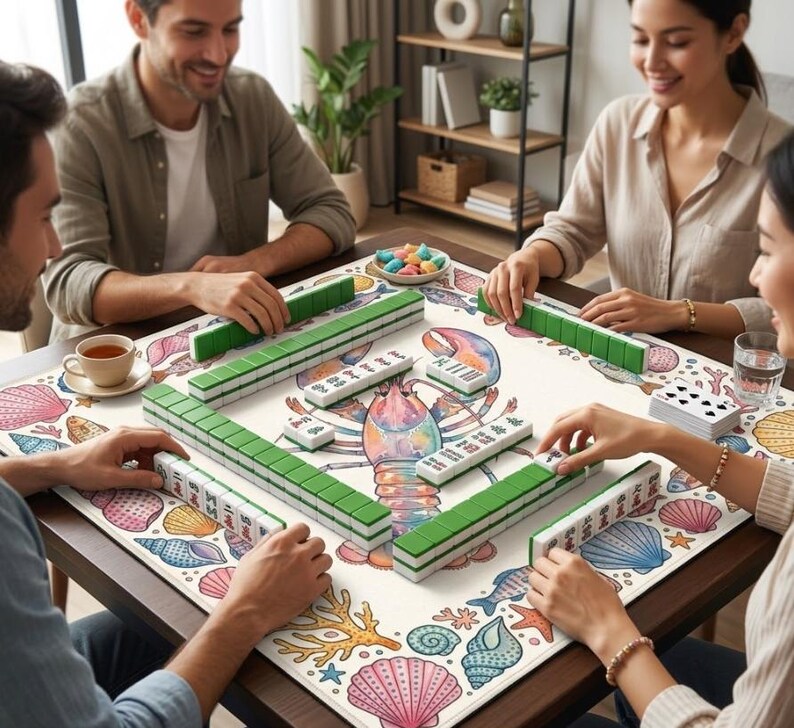 May include: A Mahjong game in progress, with green and white tiles arranged on a table. The mat features a lobster and seashell design. Players are gathered around the table, interacting with the game. A cup of tea is also visible.