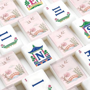 May include: A collection of white mahjong tiles featuring colorful designs. Some tiles display the letters E and N within a pagoda structure, while others show Roman numerals I, II, III, and 5, or a scenic illustration of a bridge, bamboo, and birds.