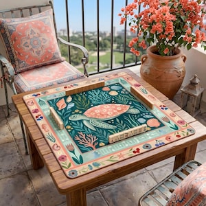 May include: A wooden table with a colorful game board featuring a sea turtle design. The board is surrounded by wooden game pieces and floral and seashell motifs. A matching pillow and chair are in the background, along with a terracotta pot with orange flowers.