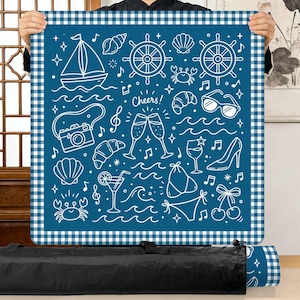 Puede incluir: Una alfombra azul con un dise&ntilde;o n&aacute;utico blanco y un borde de cuadros. La alfombra presenta dibujos lineales blancos de un velero, conchas marinas, copas de champ&aacute;n y otros iconos veraniegos. La palabra "Cheers!" tambi&eacute;n es visible.