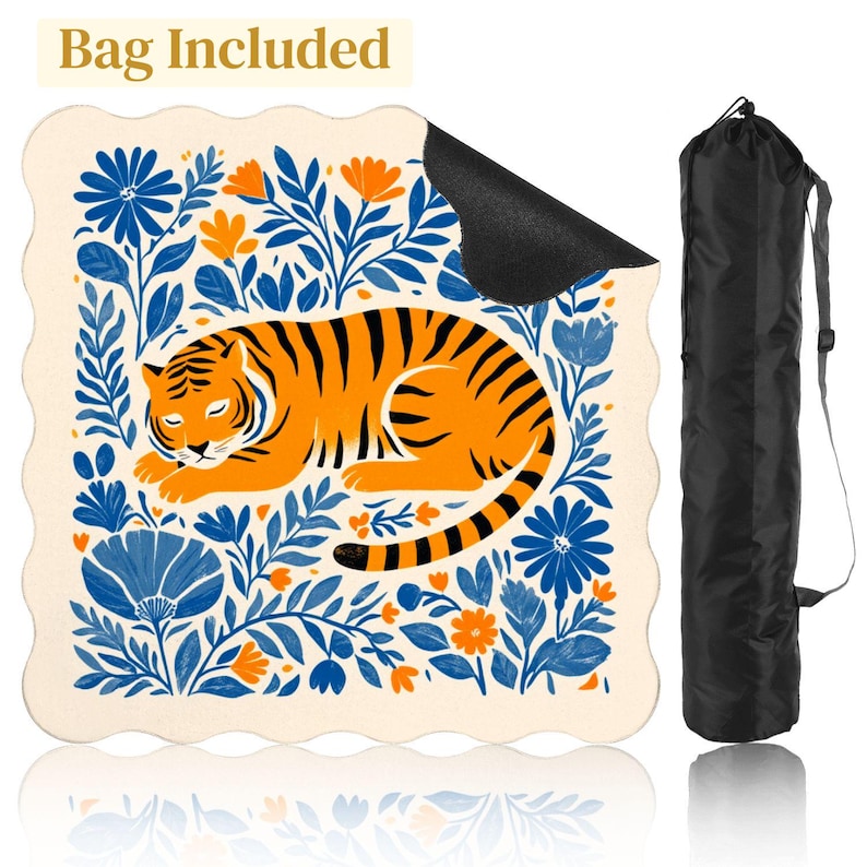 May include: A cream-colored yoga mat with a sleeping orange tiger design surrounded by blue and orange floral elements. The mat has a scalloped edge and includes a black carrying bag. Text on the top says "Bag Included".