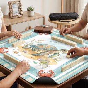 May include: A square game table with a sea turtle design. The table is covered with a blue and white mat featuring a turtle, crabs, and seashells. Players are arranging beige game tiles. A glass of water with a lemon slice is on the table.
