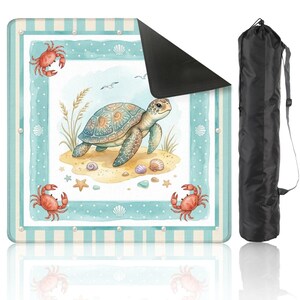 May include: A beach blanket with a watercolour design of a sea turtle on a sandy beach with seashells, starfish, and crabs. The blanket has a blue and white striped border and comes with a black carrying bag.