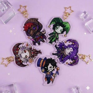 May include: Five acrylic keychains featuring cartoon characters in various costumes. The keychains have gold star-shaped clasps. The characters are dressed in outfits with colors like purple, green, red, and black. The background is a light purple.