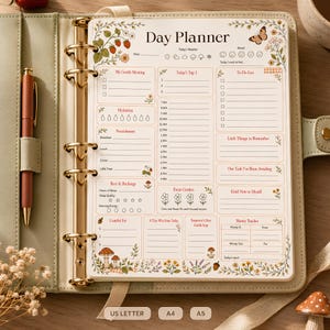 Può includere: Un'agenda ad anelli color verde salvia con un meccanismo di rilegatura in metallo dorato e una penna abbinata. La pagina dell'agenda include sezioni per meteo, umore, idratazione, pasti, un programma giornaliero dalle 7:00 alle 21:00 e un tracker finanziario, decorata con illustrazioni botaniche di fragole, funghi e una farfalla.