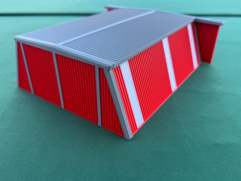 May include: A miniature red and gray model of a building with a corrugated metal roof. The building has red walls with white vertical stripes and gray trim. The model is likely for architectural or hobbyist use.