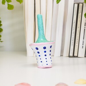 Peut inclure: Un bouchon de bouteille décoratif en céramique peint à la main. Il présente une base blanche avec des pois bleus, un bord rose et un dessus turquoise et vert. Conçu pour s'insérer dans une bouteille.