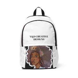 May include: White backpack with a black zipper and handle. The front features a black panel with a watercolor illustration of a woman with curly hair, flowers, and earrings. The text "V&D CREATIVE DESIGNS" is printed on the top.