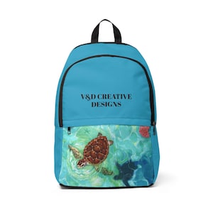 Può includere: Uno zaino turchese con cerniera e manico neri. La parte inferiore presenta un disegno ad acquerello di tartarughe marine che nuotano nell'oceano. Il testo "V&D CREATIVE DESIGNS" è stampato sullo zaino.