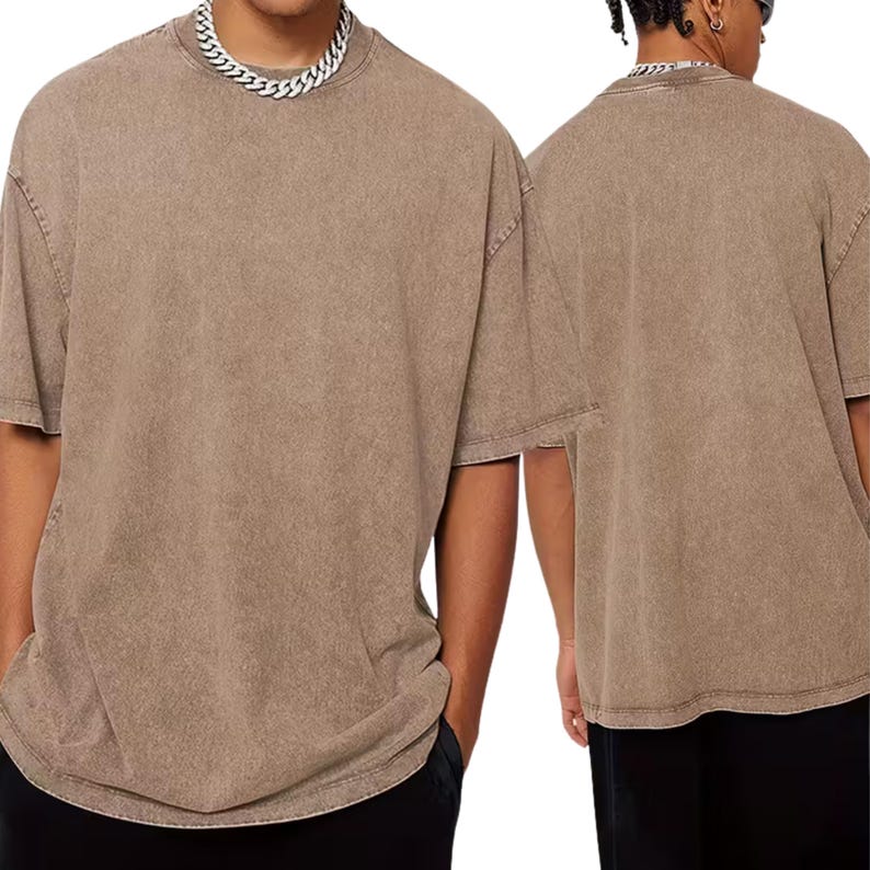 A man wearing a beige t-shirt and black pants, with a silver chain necklace.