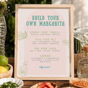 Könnte beinhalten: Ein gerahmtes Schild mit dem Text "Build Your Own Margarita" in Grün und Weiß. Das Schild listet Optionen für Tequila, Mix, Rand und Garnitur auf. Zutaten wie Limetten, Erdbeeren und Jalapeños werden in der Nähe angezeigt.
