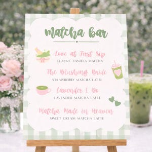 May include: A wooden easel displays a sign with the words "Matcha Bar" in green script. The sign lists matcha latte flavors: Classic Vanilla, Strawberry, Lavender, and Sweet Cream. A glass of matcha drink is visible.