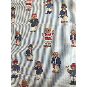 May include: A white fabric with thin vertical blue stripes featuring a repeating pattern of brown teddy bears dressed in various outfits, including blazers, sweaters, and hats, with some bears holding sports equipment like polo mallets.
