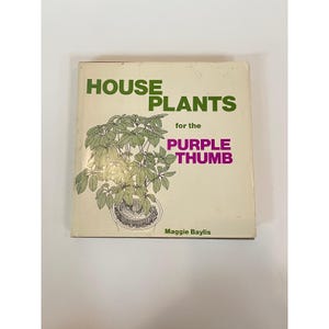 May include: A white ceramic mug with a black handle and the text "But First, Coffee" in a bold, black font. The mug is set against a blurred background, suggesting a cozy setting.