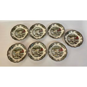 May include: A set of seven round ceramic bowls featuring a detailed transferware scene of a winter landscape with a red building, bare trees, and a stream. Each bowl has a scalloped edge with a dark green decorative border pattern.