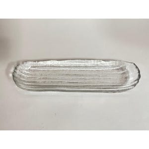 May include: A clear, rectangular glass serving tray with a textured, ridged surface. The tray has rounded edges and is designed for serving food or displaying items. The glass is transparent, allowing visibility of the surface beneath.
