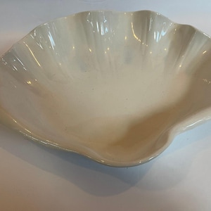May include: A cream-colored, shell-shaped serving dish. The dish has a scalloped edge and a glossy finish. The interior is smooth and the overall design is reminiscent of a seashell. This decorative dish is suitable for serving appetizers or displaying decorative items.