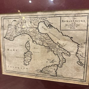Può includere: Un'antica mappa dell'Impero Romano nella sua età giovanile, secondo Floro. La mappa è in bianco e nero, che mostra la penisola italiana e le aree circostanti. La mappa è incorniciata in una cornice rosso scuro.