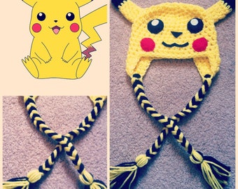 May include: A yellow crocheted hat resembling Pikachu, featuring black-tipped ears, black eyes, red cheek circles, and a smiling mouth. The hat has two braided tassels in black and yellow.