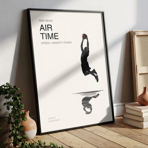 Può includere: Stampa artistica incorniciata con un giocatore di basket a mezz'aria. Le parole "AIR TIME" sono sopra il giocatore, con "SPEED • HEIGHT • FINISH" sotto. La frase "GRAVITY DISAPPEARS" è in basso.