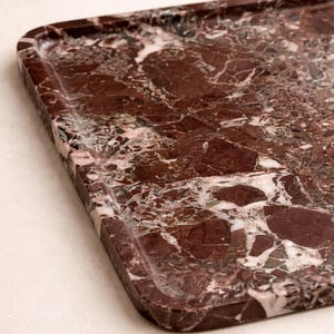 May include: A rectangular serving tray with a raised edge, made from polished red marble. The marble has a complex pattern of dark red, white, and grey veining, creating a luxurious aesthetic. Suitable for serving food or displaying decorative items.