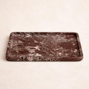 May include: A rectangular serving tray made of red marble with white veining. The tray has a slightly raised edge and rounded corners. This decorative tray is suitable for serving food or displaying items.