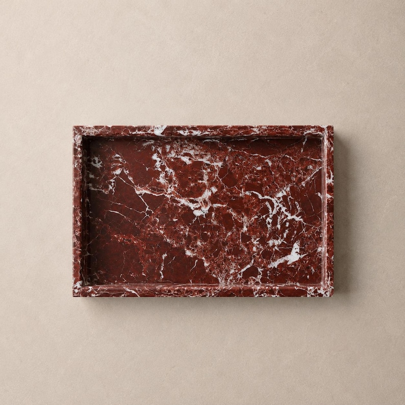 May include: A rectangular tray crafted from deep red marble featuring prominent white veining throughout the surface. The tray has a raised border and a smooth, polished finish, showcasing the natural stone pattern with a consistent color palette.