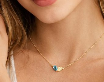 May include: A delicate gold necklace featuring two teardrop-shaped gemstones, one blue and one yellow. The gemstones are set close together on a fine gold chain. The necklace is worn around the neck.