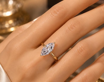 May include: A gold ring featuring a single marquise-cut clear gemstone set in a four-prong setting. The band is thin and polished, showcasing a reflective metallic finish that complements the faceted stone centered on the finger.