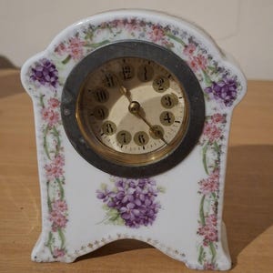 porcelain mantel clock featuring a white ceramic body decorated with transfer-ware patterns of purple violets and pink floral vines.