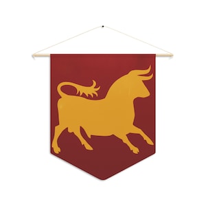 May include: A burgundy wall banner with a gold silhouette of a bull. The banner is rectangular with a pointed bottom and is suspended from a wooden dowel with a string for hanging. The bull is depicted in a running pose.