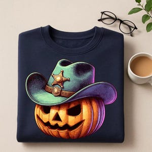 May include: Navy blue sweatshirt featuring a Halloween-themed design. The graphic depicts a jack-o'-lantern wearing a green and purple cowboy hat with a sheriff's badge. The pumpkin is orange with a carved face. A fun and festive design for the spooky season.