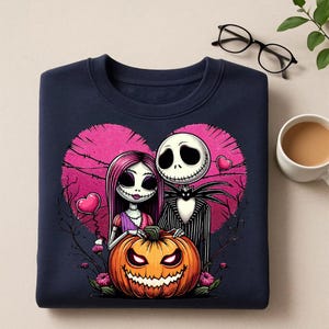 May include: Navy blue sweatshirt featuring a Halloween-themed design. The graphic includes a couple with a pumpkin, set against a pink heart backdrop. The pumpkin has a carved face. The design is a cartoon style.
