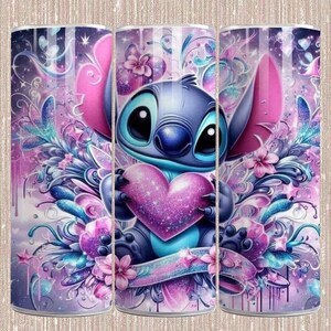 May include: A tumbler featuring a cartoon character holding a heart. The design is predominantly purple, pink, and blue, with floral and star accents. The character has large ears and a blue body. The background has a dreamy, glittery effect.
