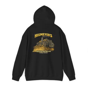 May include: Black hooded sweatshirt with a graphic of a bulldozer and the text "HEEMEYER'S MOUNTAIN VIEW MUFFLERS Granby, Colorado" in yellow. The hoodie has a drawstring and a kangaroo pocket.
