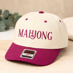 Peut inclure: Une casquette de baseball crème avec une visière magenta foncé et le texte brodé MAHJONG sur le devant. La casquette présente un petit autocollant sur la visière avec le texte OTTO CLASSIC FIT OSFM MID PROFILE.