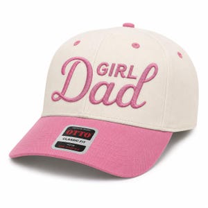 Könnte beinhalten: Eine cremefarbene Baseballkappe mit rosafarbenem Schirm und rosafarbener Stickerei mit der Aufschrift "Girl Dad" auf der Vorderseite. Die Kappe hat eine strukturierte Krone mit passenden rosafarbenen Ösen und einen Aufkleber auf dem Schirm.
