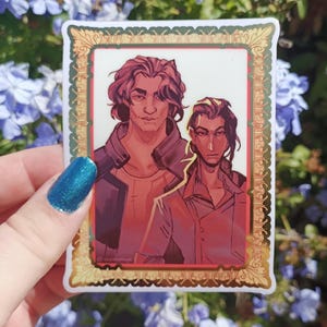 Puede incluir: Una pegatina con una ilustración digital de dos figuras con pelo largo, enmarcada en oro y verde. Las figuras están representadas en tonos rojos y marrones, con un estilo artístico detallado.