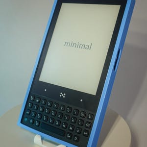 May include: An electronic device with a blue frame, black keyboard, and screen displaying the word "minimal". The device is supported by a white stand. The screen is rectangular. The device has a keyboard.