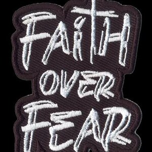 May include: Embroidered patch with the words "Faith Over Fear" in white script. The patch has a dark brown background with a white border and a cross incorporated into the design.