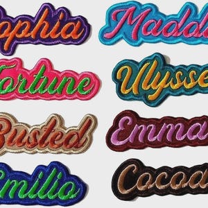 May include: A collection of embroidered name patches in various colors. The names include "Sophia", "Maddie", "Fortune", "Ulysse", "Busted", "Emma", "Emilio", and "Cocoa". Each patch features a unique color scheme and font style, with a contrasting border.