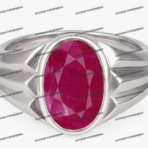 May include: A silver-toned ring featuring a large, oval-cut, deep pinkish-red gemstone set in a smooth bezel. The band has a wide, polished metallic finish with distinct geometric, angular facets on both sides of the central stone setting.