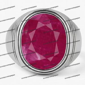 Puede incluir: Un anillo de tono plateado con una gran piedra preciosa de corte ovalado en color rojo rosado intenso, engastada en una banda de metal liso y pulido. La piedra muestra una superficie facetada con un patrón estelar que refleja luz.