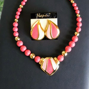 Pu&ograve; includere: Una collana rosa e oro con un ciondolo geometrico e orecchini abbinati. La collana &egrave; realizzata con perline rosa e dettagli dorati. Anche gli orecchini sono rosa e oro con un design geometrico. L'etichetta sulla collana recita "Napier Original Napier".