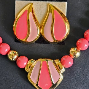 Pu&ograve; includere: Un set di collana e orecchini rosa e oro di Napier. La collana presenta un grande ciondolo geometrico con accenti rosa e oro. Gli orecchini sono a forma di goccia con accenti rosa e oro.
