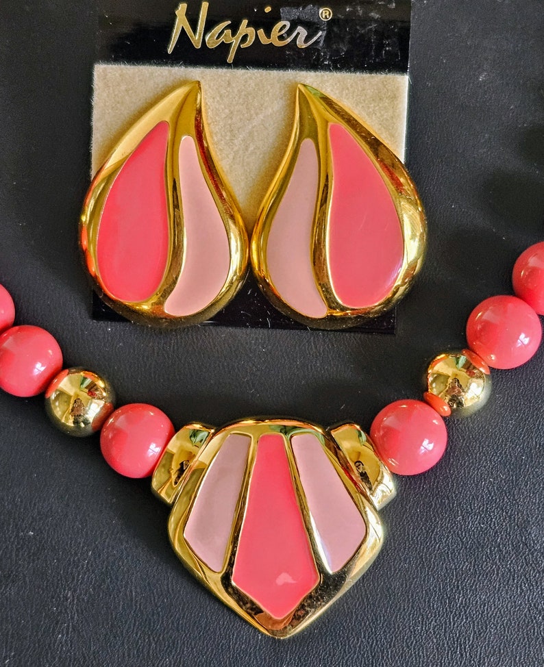 Pu&ograve; includere: Un set di collana e orecchini rosa e oro di Napier. La collana presenta un grande ciondolo geometrico con accenti rosa e oro. Gli orecchini sono a forma di goccia con accenti rosa e oro.