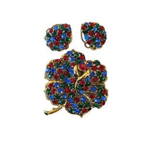 Pode incluir: Um conjunto de broche e brincos em tom dourado com um design floral adornado com pedras de imita&ccedil;&atilde;o vermelhas, azuis e verdes.