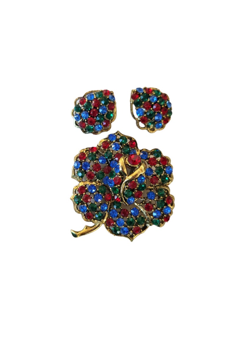 Pode incluir: Um conjunto de broche e brincos em tom dourado com um design floral adornado com pedras de imita&ccedil;&atilde;o vermelhas, azuis e verdes.